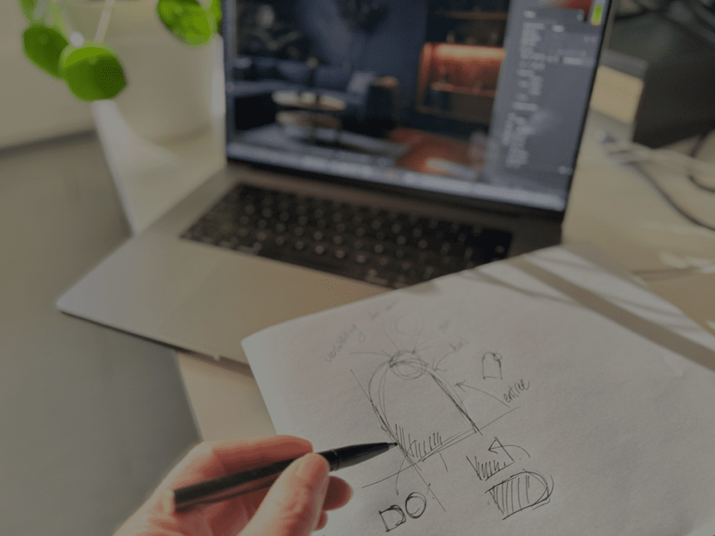Hand met potlood schetst een ontwerp op papier naast een laptop met grafisch ontwerp op het scherm.