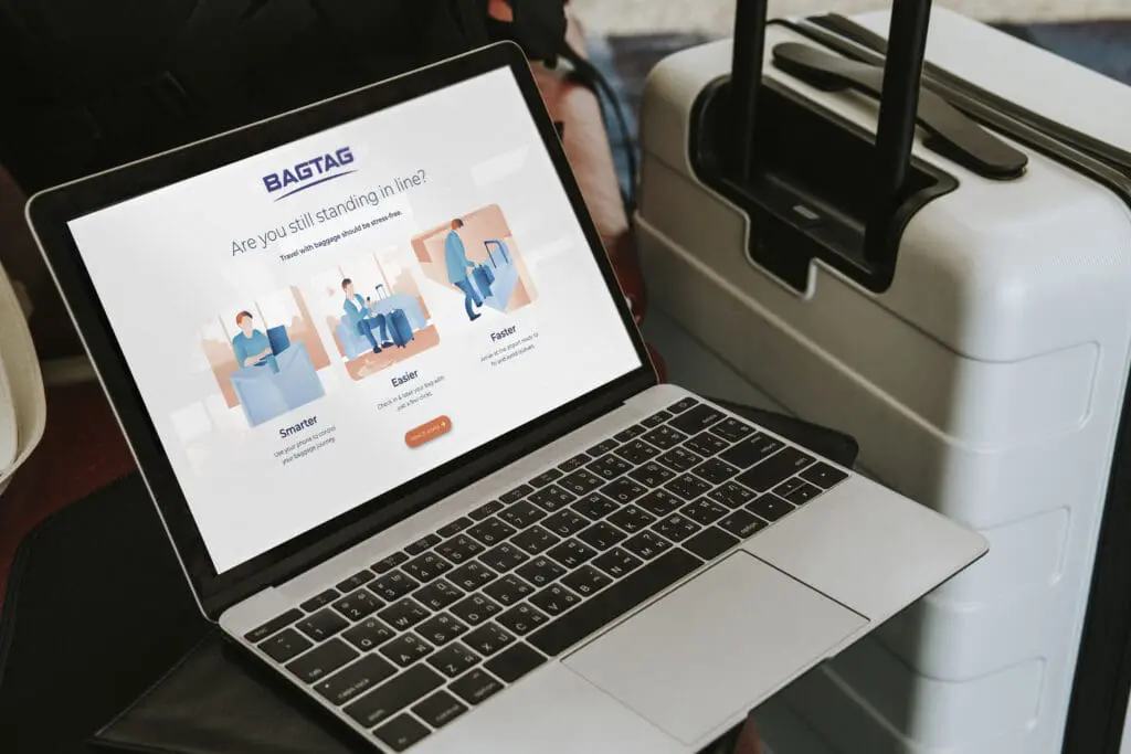 Laptop met BAGTAG-website naast een koffer in een reisomgeving.