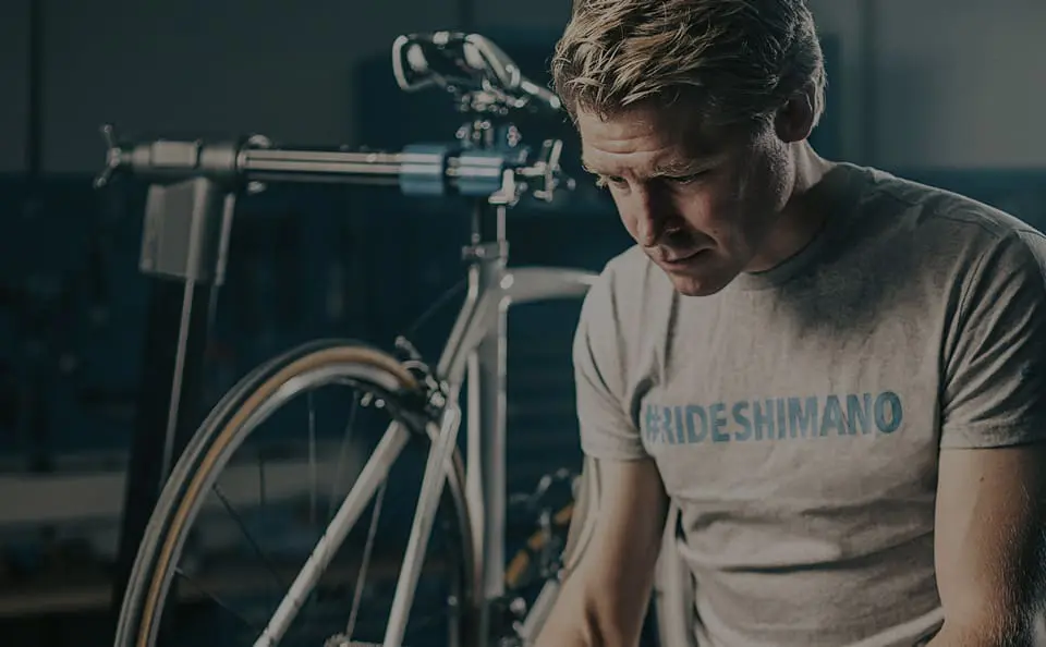 Fietsmonteur van Shimano is bezig in de werkplaats terwijl een racefiets op de achtergrond staat.