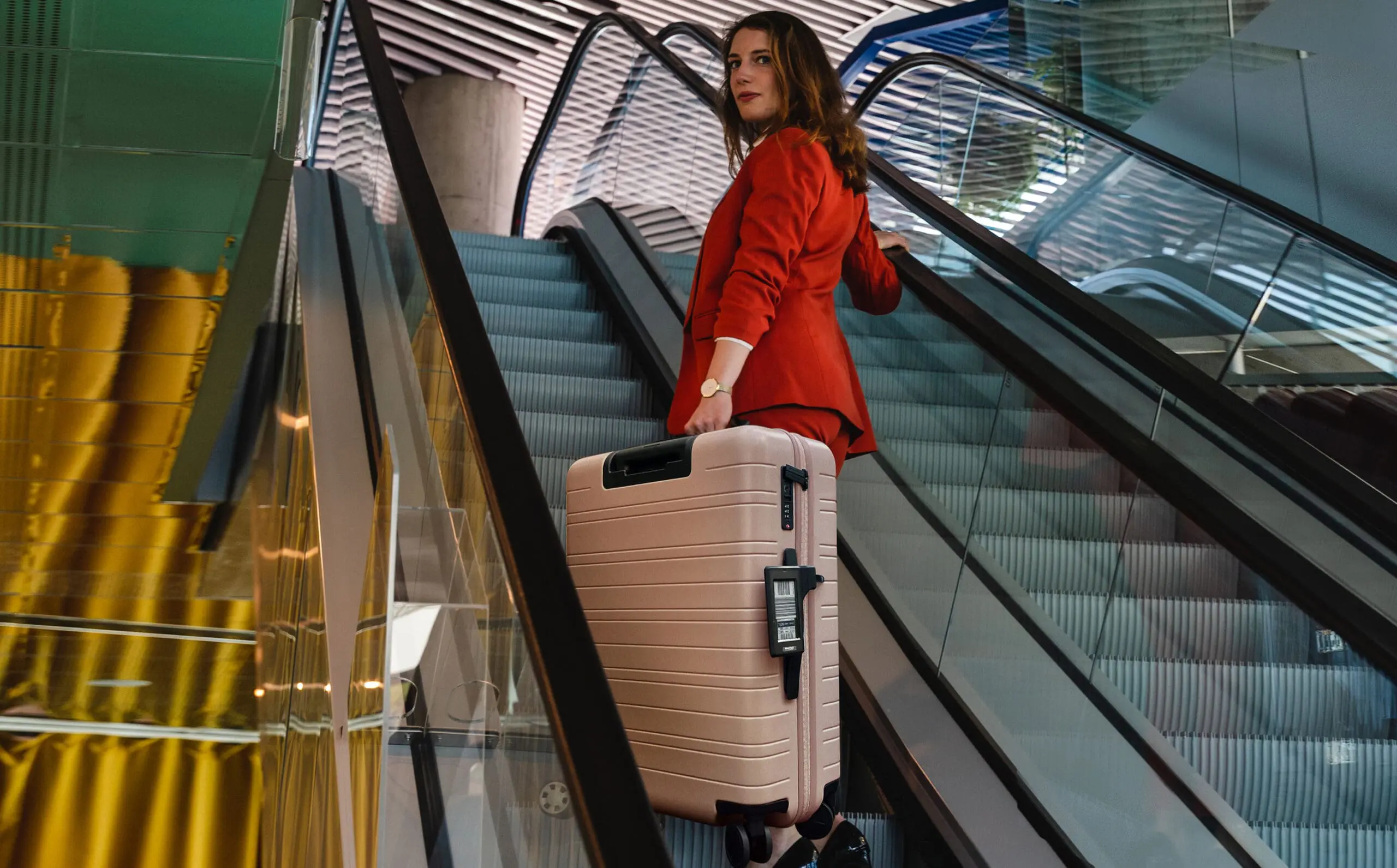 Vrouw met koffer met Bagtag staat op een roltrap in een modern gebouw.