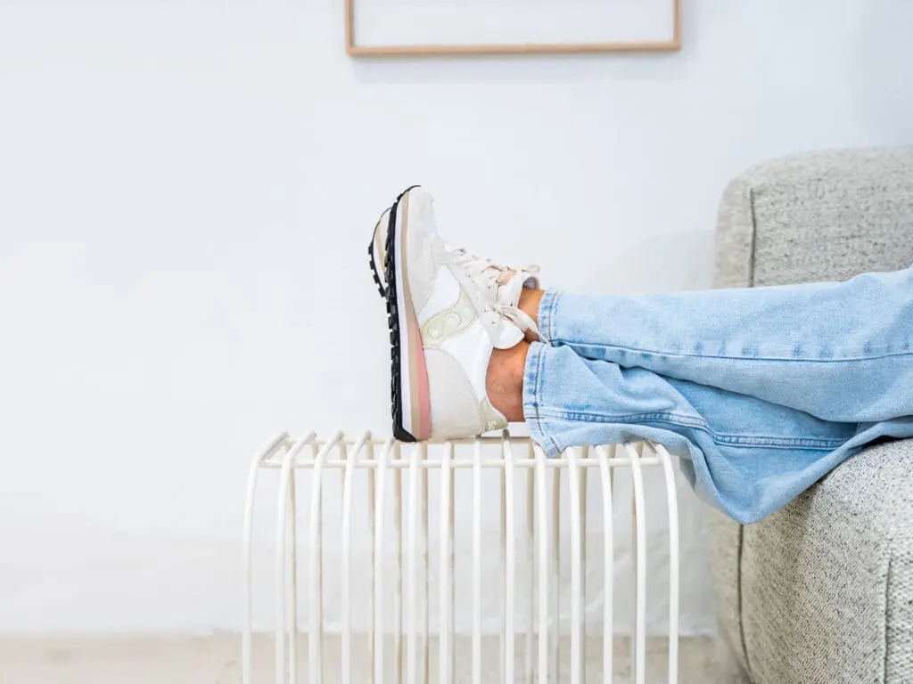 Persoon met sneakers en spijkerbroek legt benen ontspannen op een kleine metalen bijzettafel.