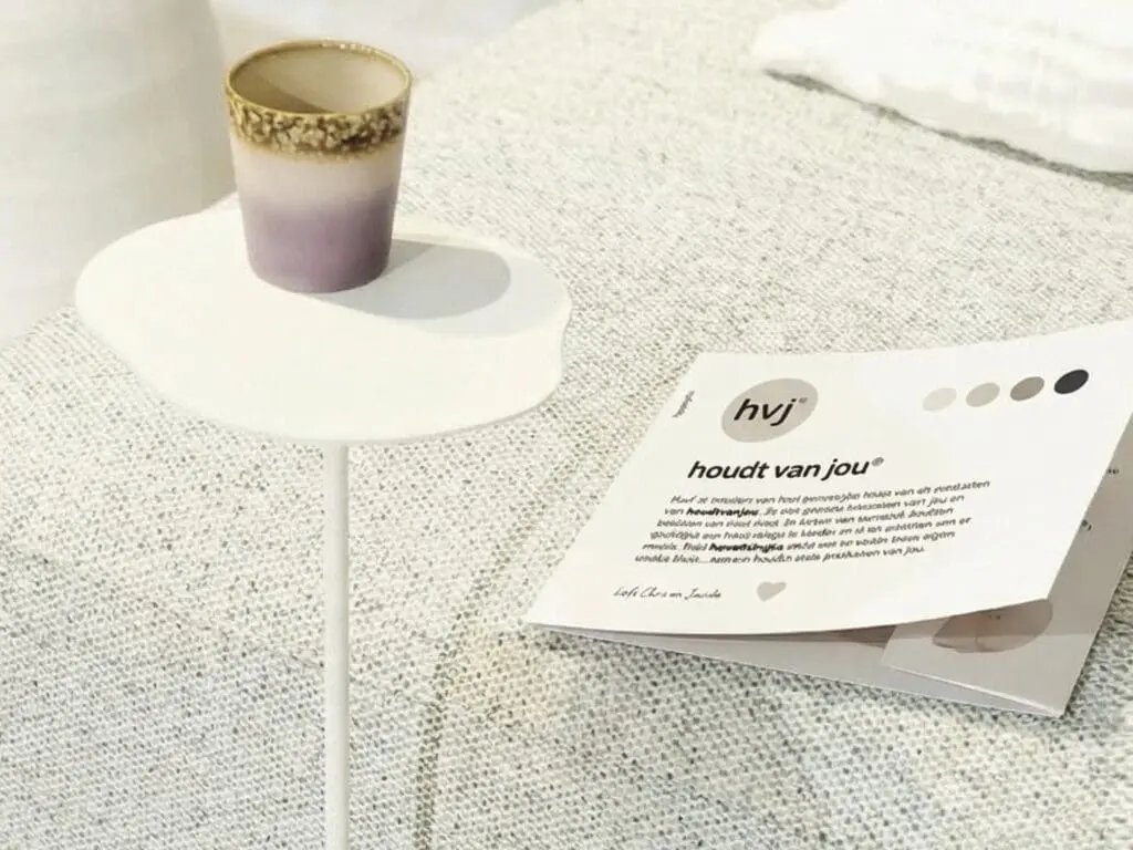 Productkaart met hvj-huisstijl ligt op een lichte bank naast een bijzettafel met keramische beker.