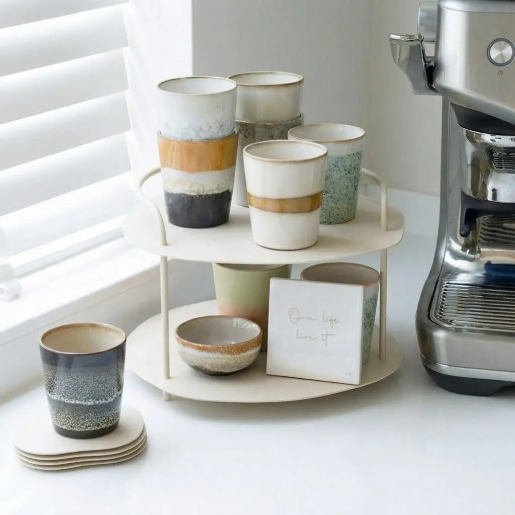Servies van HVJ met mokken en schaaltjes op een klein rek naast een koffiemachine.