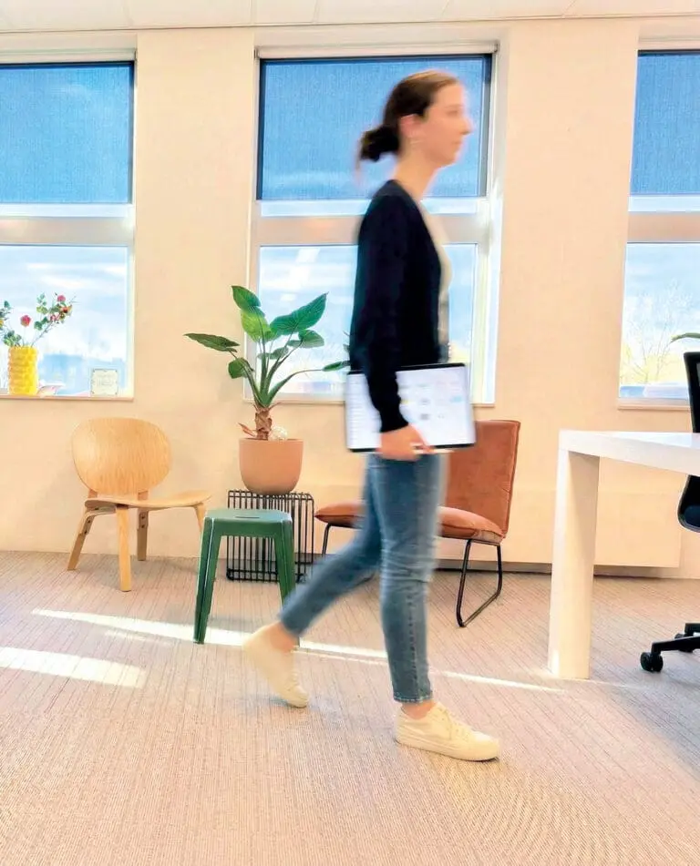 Medewerker van Loeks loopt door een lichte kantoorruimte met planten en werkplekken.