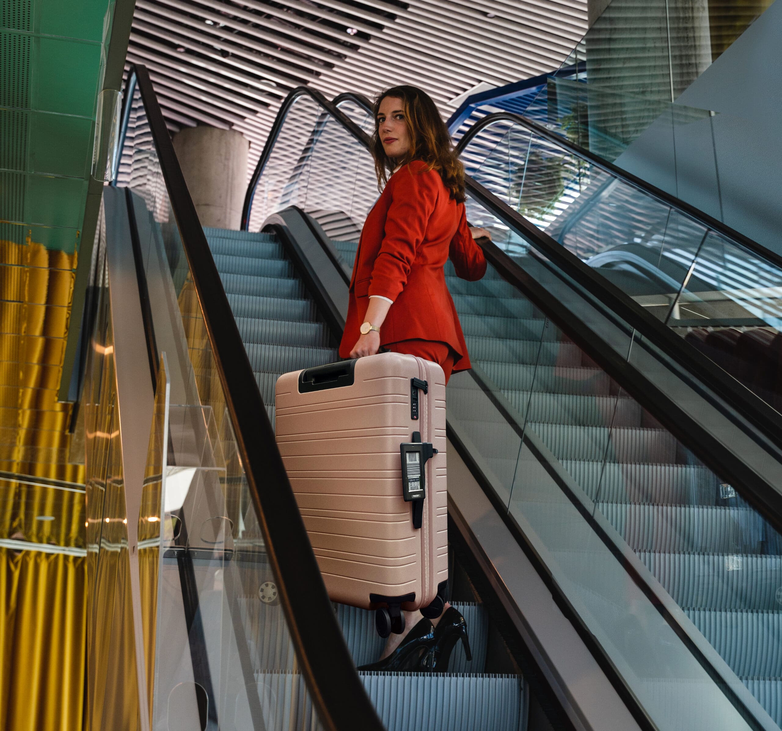 Vrouw met koffer met Bagtag staat op een roltrap in een modern gebouw.