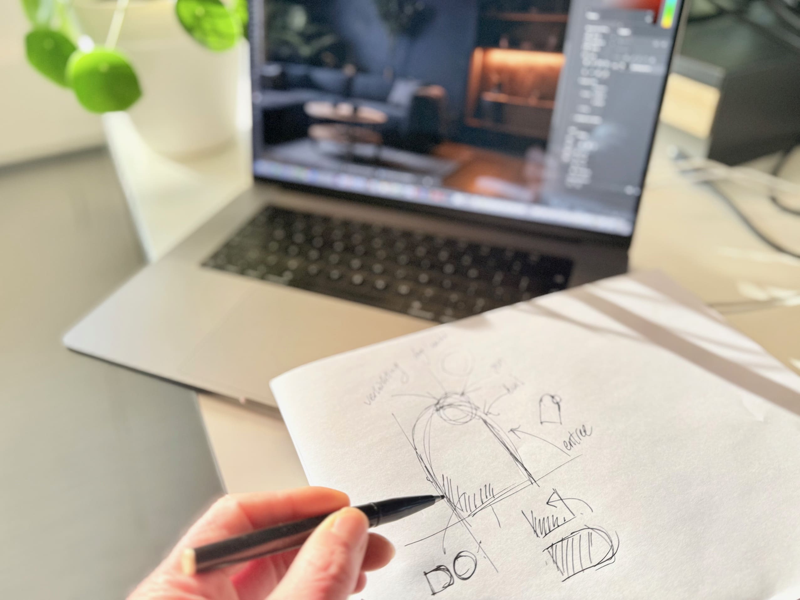 Hand met potlood schetst een ontwerp op papier naast een laptop met grafisch ontwerp op het scherm.