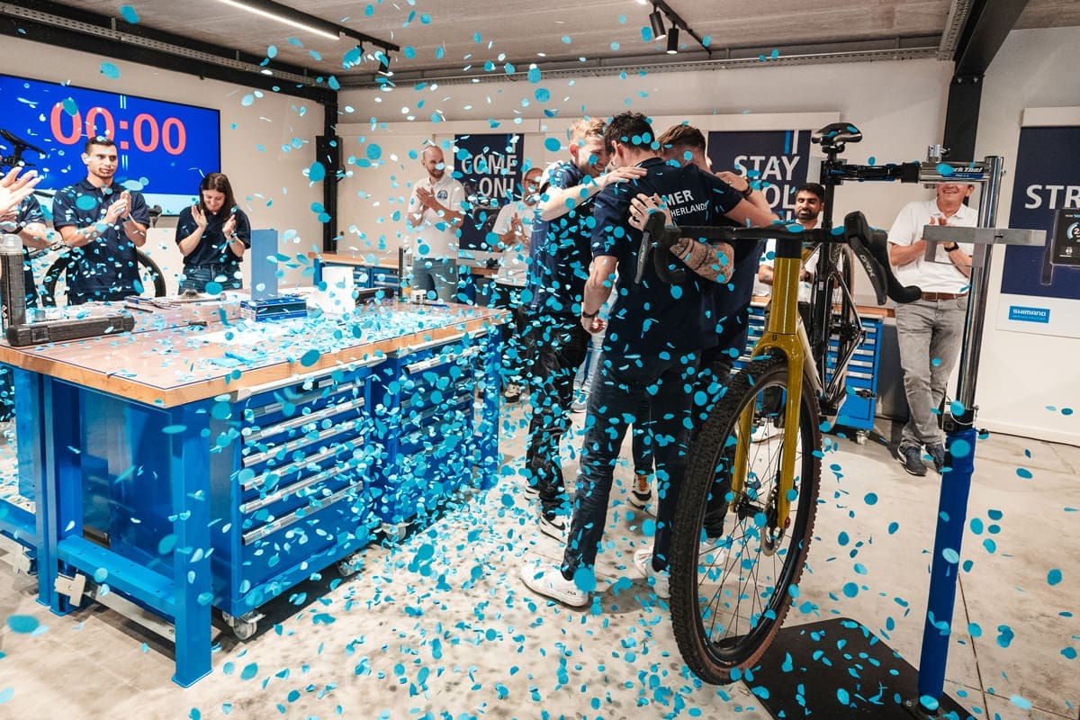 Team van Shimano viert samen een moment in een werkplaats terwijl blauwe confetti door de ruimte valt en collega’s applaudisseren.