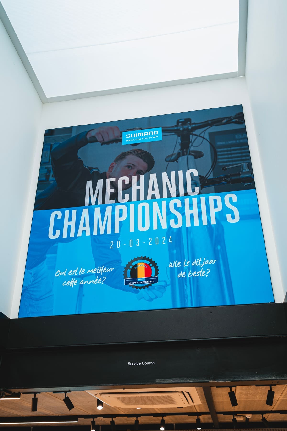 Grote poster van de Shimano Mechanic Championships met een fietstechnicus die aan een fiets werkt en informatie over het evenement op 20-03-2024.