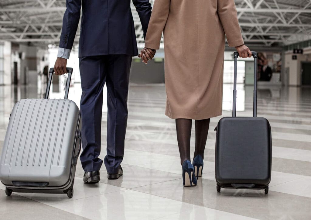 Man en vrouw lopen hand in hand door een luchthaven met rolkoffers.