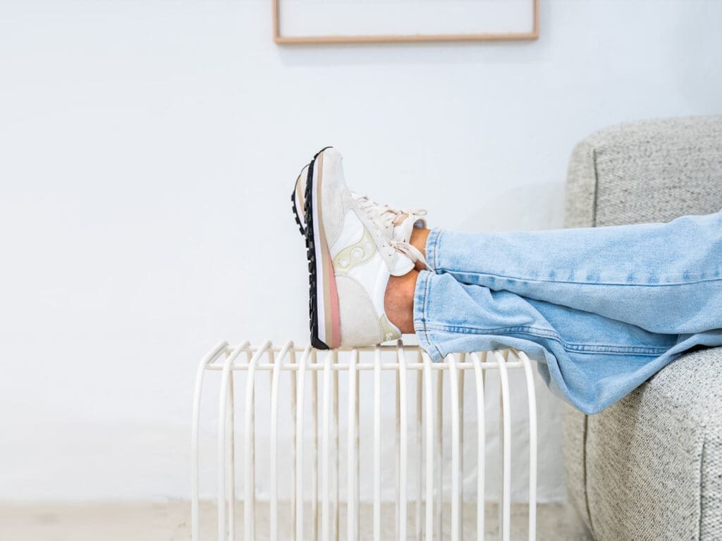 Persoon met sneakers en spijkerbroek legt benen ontspannen op een kleine metalen bijzettafel.