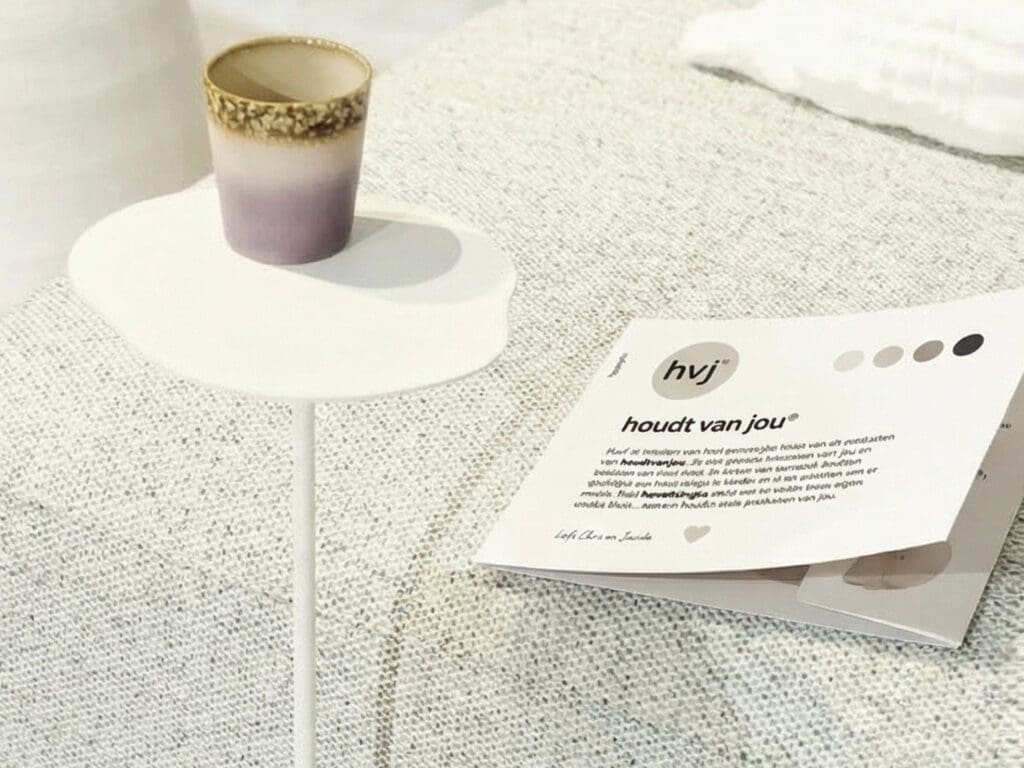Productkaart met hvj-huisstijl ligt op een lichte bank naast een bijzettafel met keramische beker.