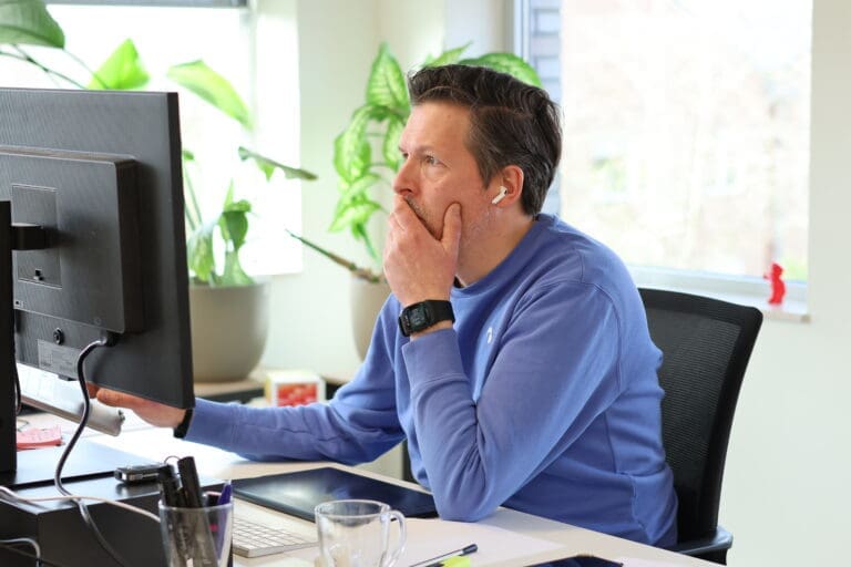 Eigenaar van Loeks werkt geconcentreerd achter een computerscherm in een lichte kantoorruimte met planten op de achtergrond.