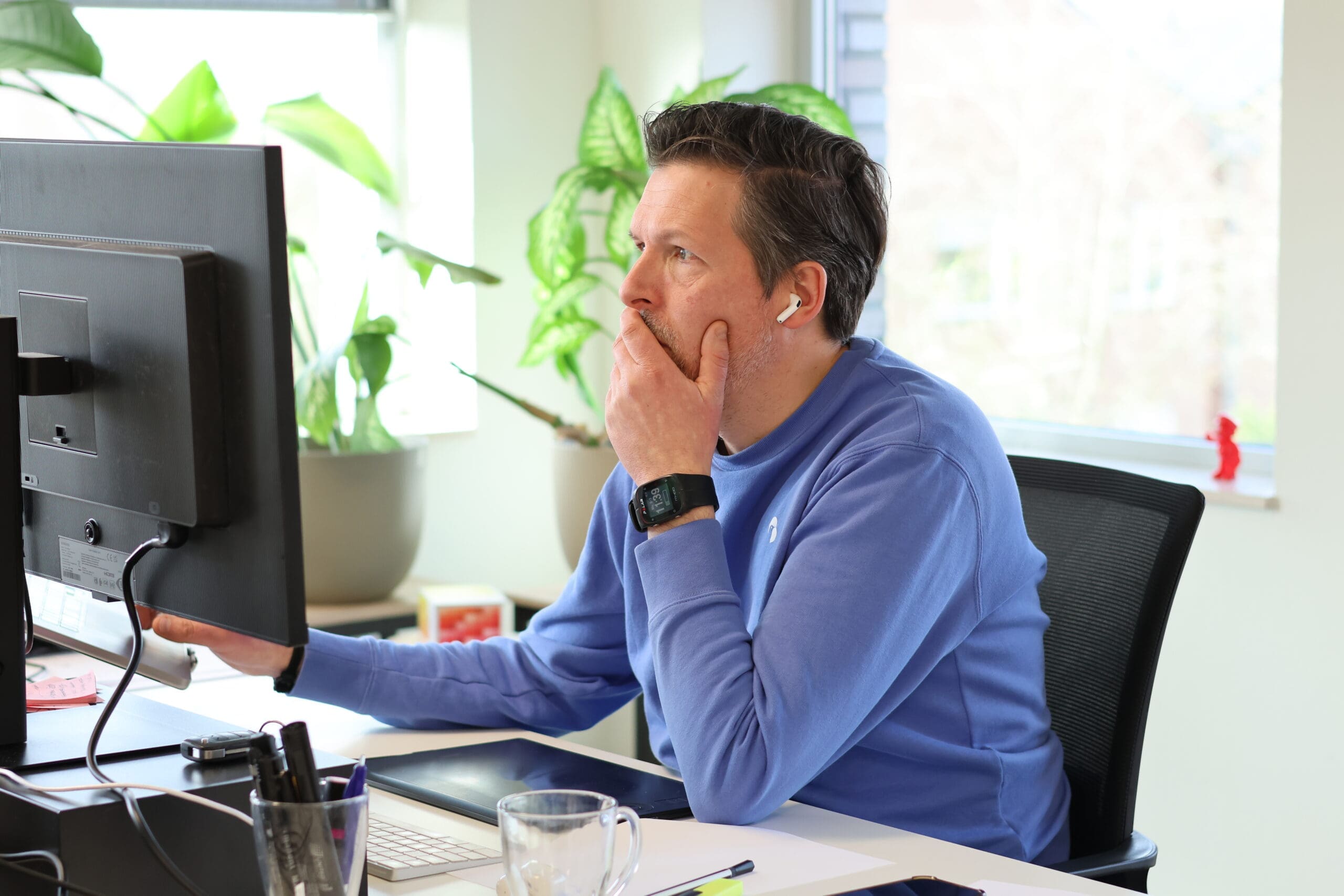 Eigenaar van Loeks werkt geconcentreerd achter een computerscherm in een lichte kantoorruimte met planten op de achtergrond.