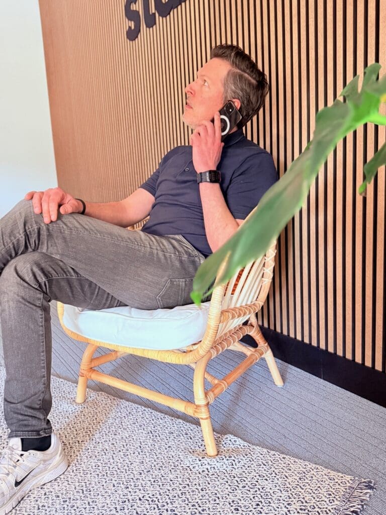 Eigenaar van Loeks voert een telefoongesprek met een potentiële klant terwijl hij in een rieten stoel zit.