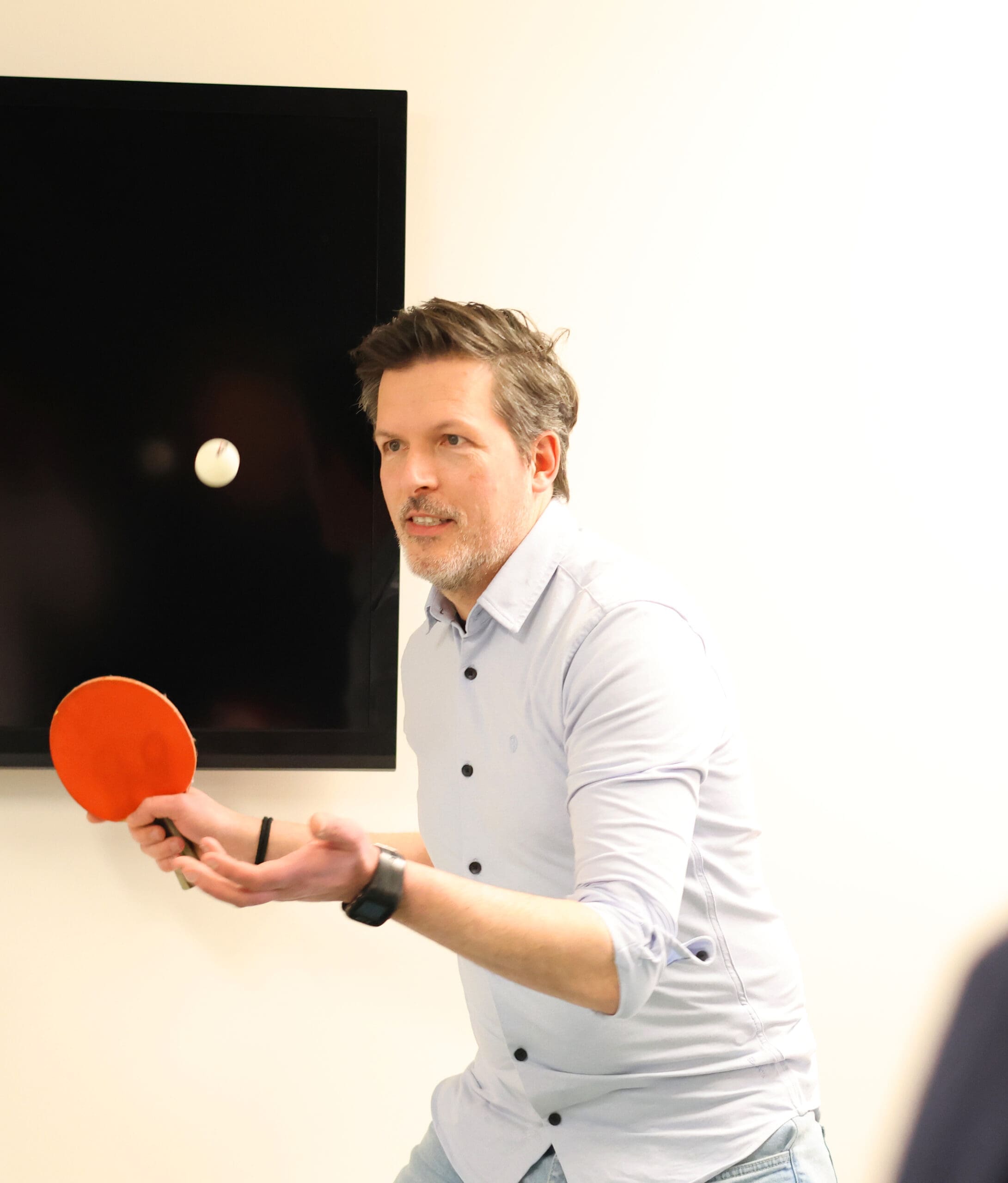Eigenaar van Loeks houdt een tafeltennisbatje vast en speelt tafeltennis in een kantoorruimte.