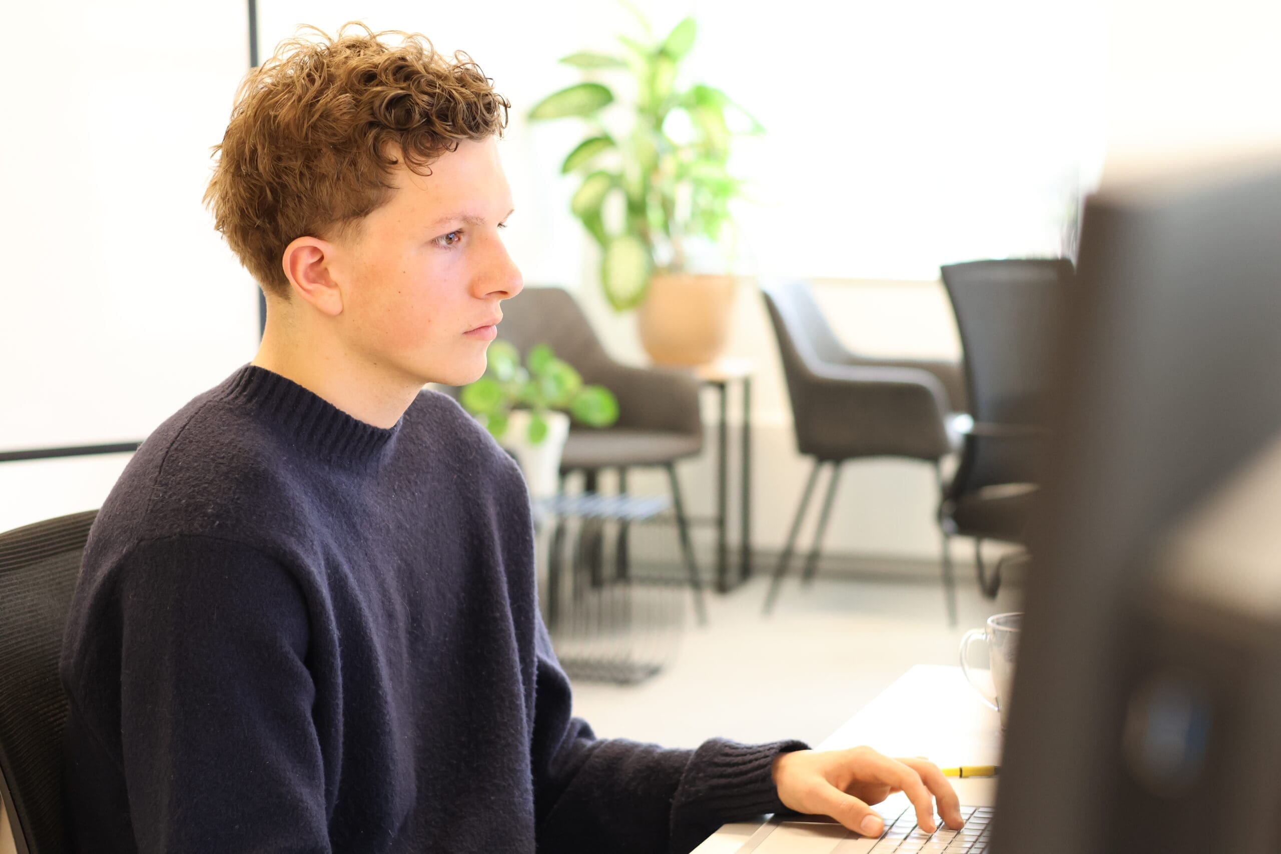 junior online marketeer van LOEKS werkt geconcentreerd achter een computerscherm in een lichte kantoorruimte met planten op de achtergrond.