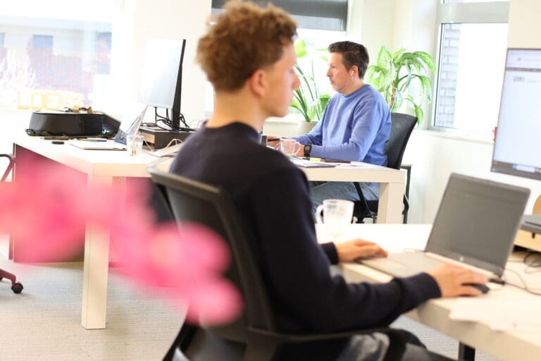 Werkruimte bij Loeks met bureaus, computerschermen en medewerkers.